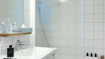 A modern bathroom with a white sink, a mirror, and a shower area.