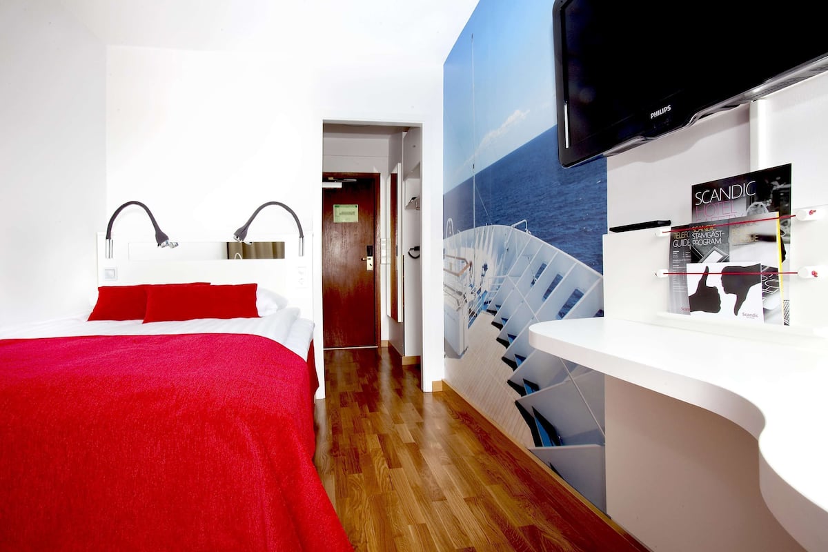 A hotel room with a bed, a desk, a television, and a mural of a ship.