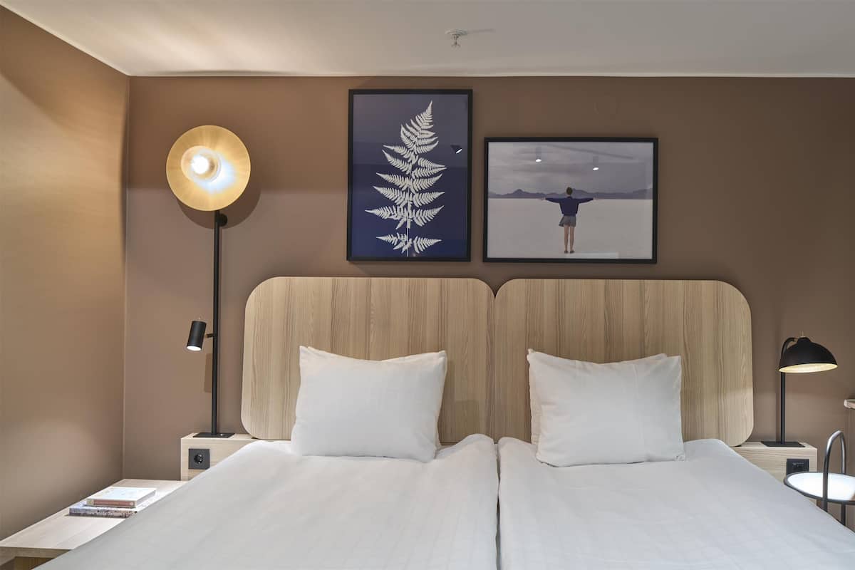 A hotel room with a large bed, two nightstands, a floor lamp, and two framed pictures on the wall.