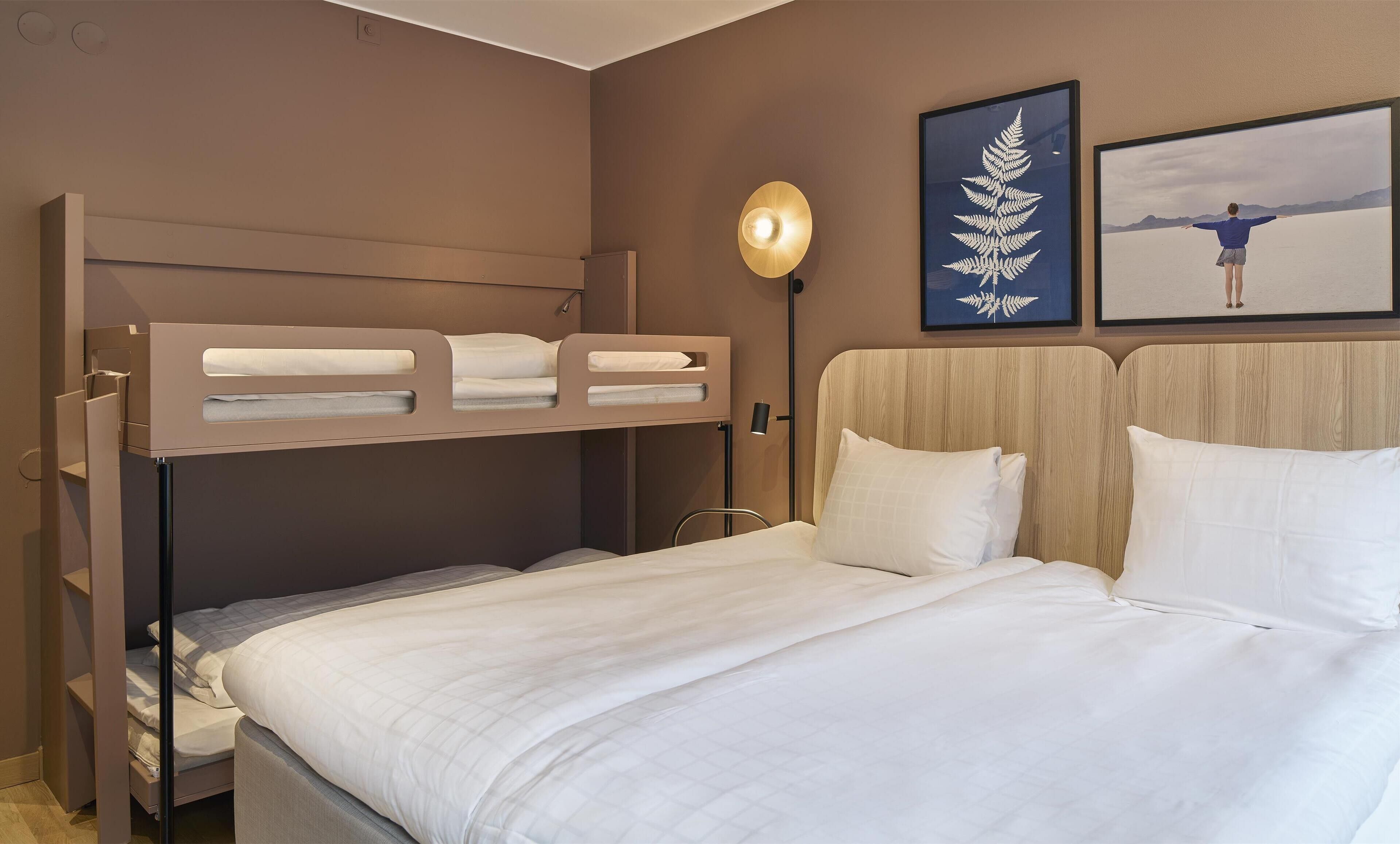 Habitación de hotel con literas, una cama individual, mesita de noche, lámpara y cuadros en la pared.