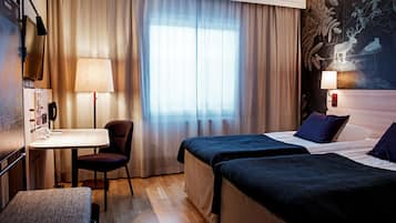 Habitación de hotel con dos camas, un escritorio con silla, una lámpara y un ventanal con cortinas.