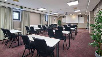 Un salón de conferencias con varias mesas y sillas, una pantalla de proyector y un amplio ventanal con cortinas.