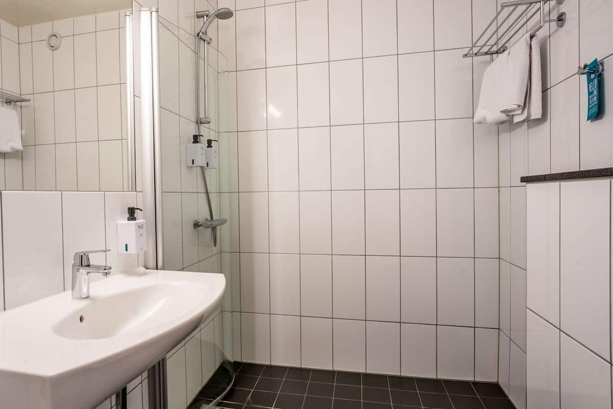 A bathroom with a white sink, a shower, and a tiled floor.