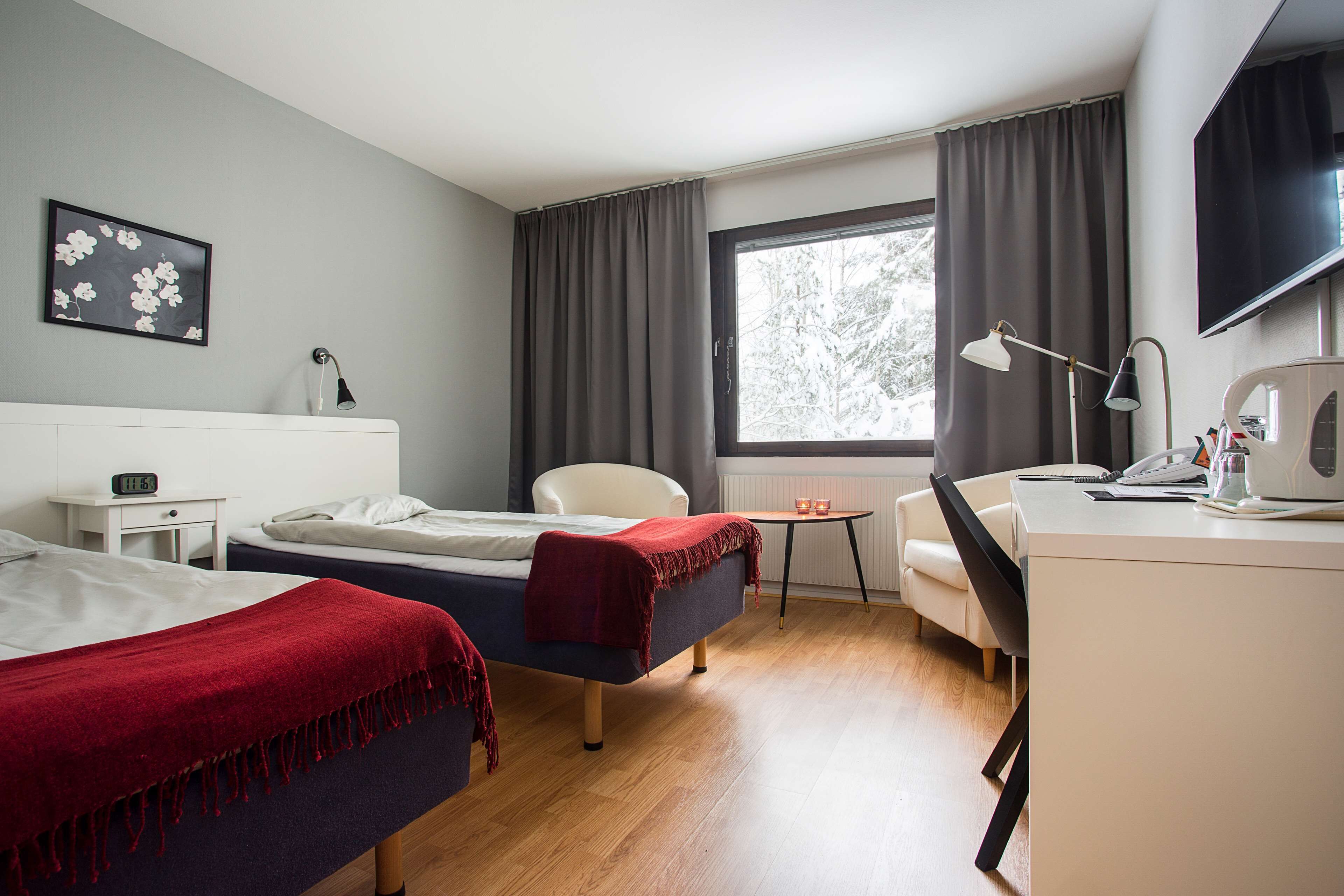 Ein Hotelzimmer mit zwei Betten, einem Schreibtisch, einem Sessel, einem Fernseher und einem Fenster mit Vorhängen.