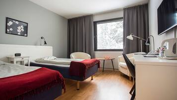 Ein Hotelzimmer mit zwei Betten, einem Schreibtisch, einem Sessel, einem Fernseher und einem Fenster mit Vorhängen.