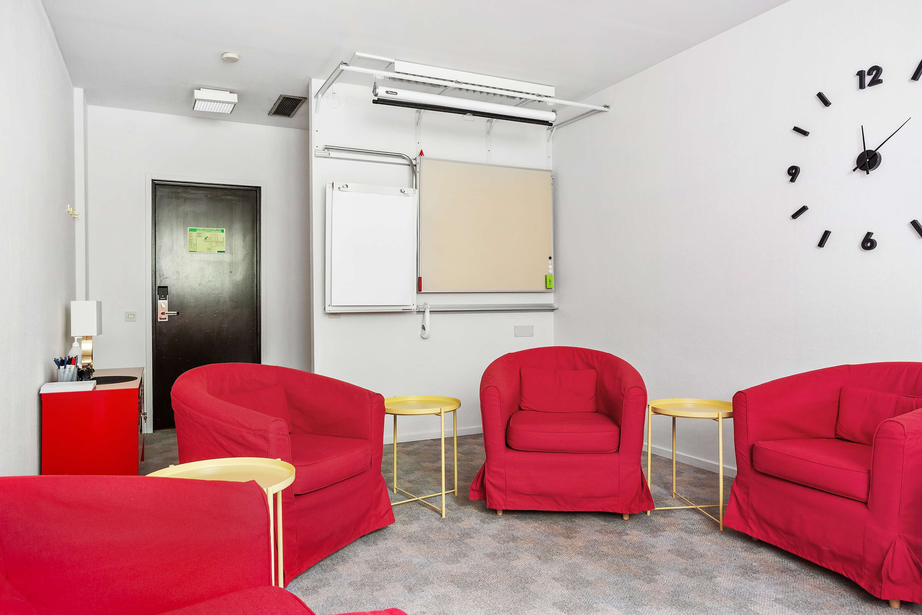 Una habitación moderna con sillas rojas, una pizarra y un reloj en la pared.