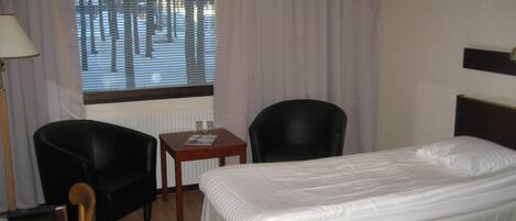 A hotel room with two beds, a desk, a chair, and a window with blinds.