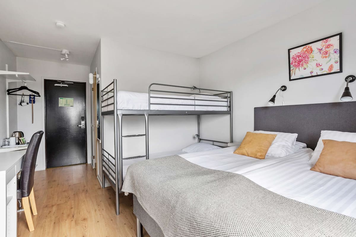 A bunk bed room with a desk and chair, a black door, and a framed floral artwork on the wall.