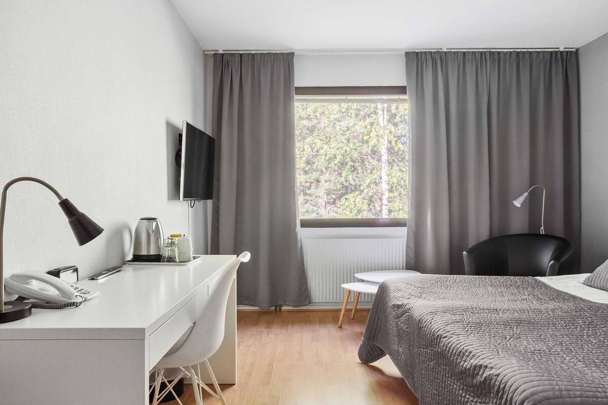 A hotel room with a desk, chair, bed, and a window with curtains.