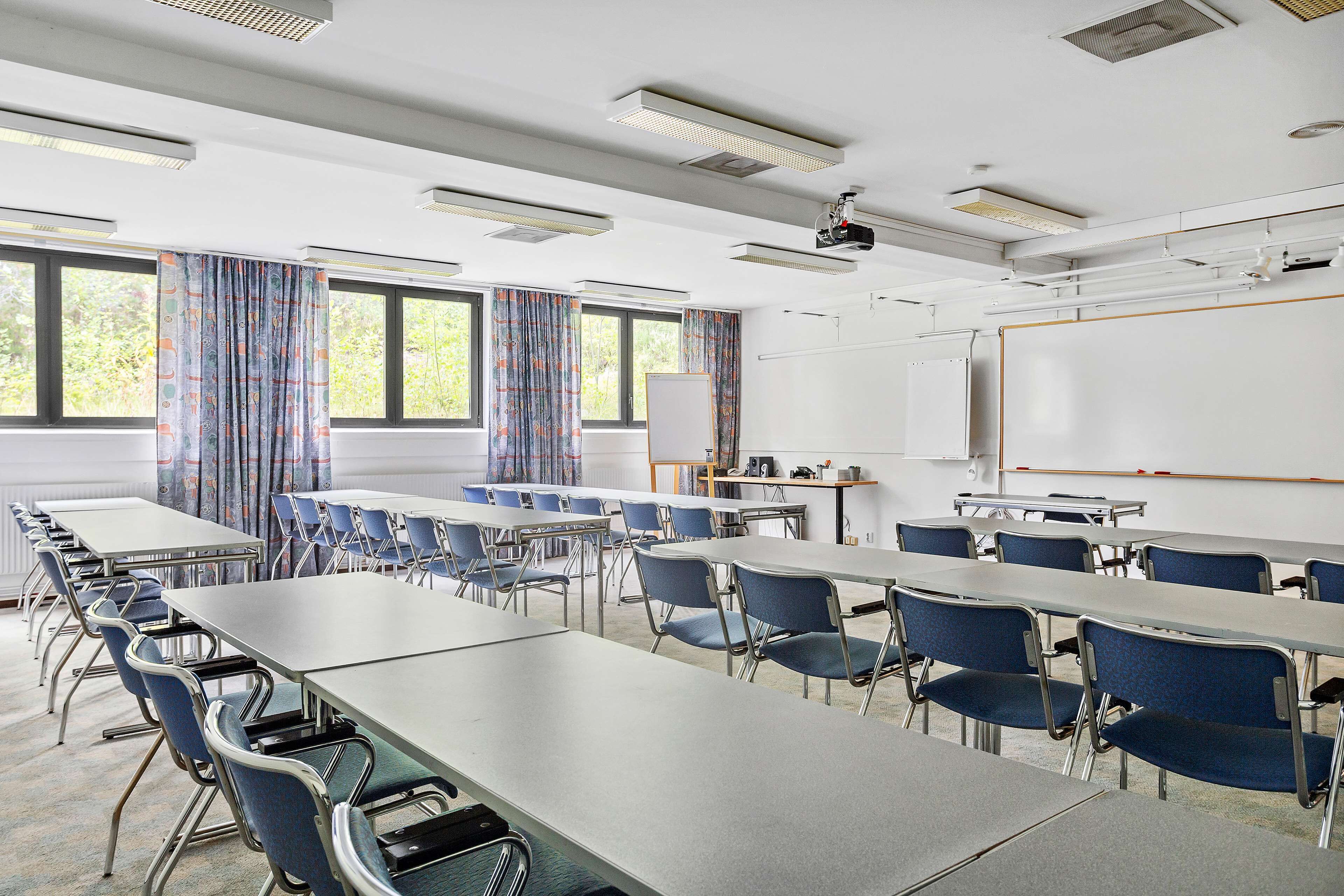 A conference room with multiple tables and chairs, a whiteboard, and a projector screen.