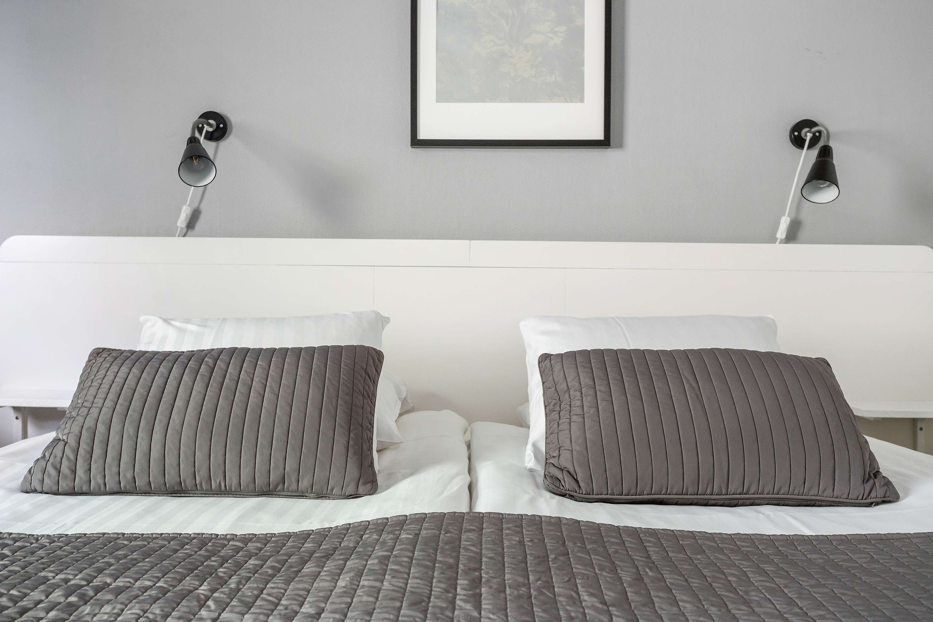 Una cama bien hecha con una colcha gris acolchada y dos almohadas grises.