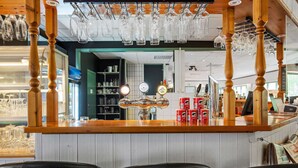 Un espace bar avec des tabourets de bar en bois, un comptoir avec de la verrerie et des étagères remplies de bouteilles.