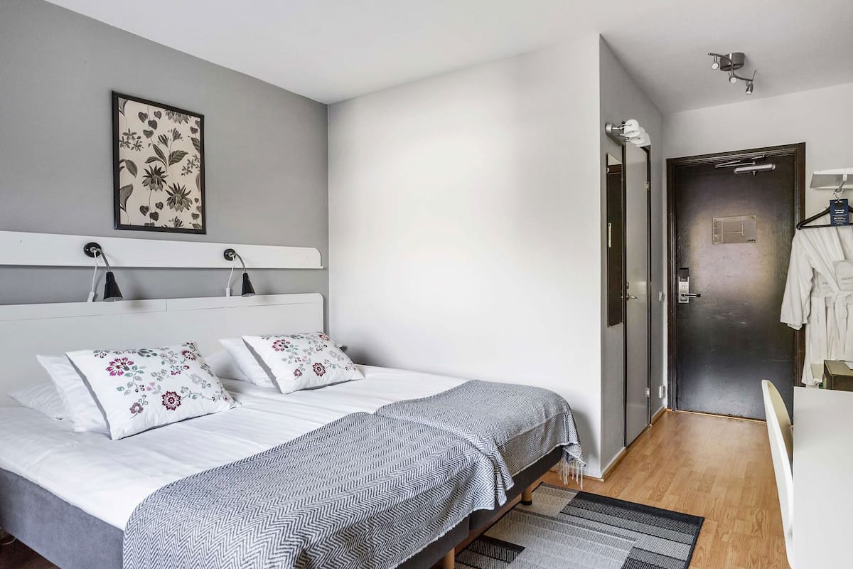 A modern bedroom with a bed, bedside lamps, a framed floral artwork, a door with a towel rack, and a visible bathroom.