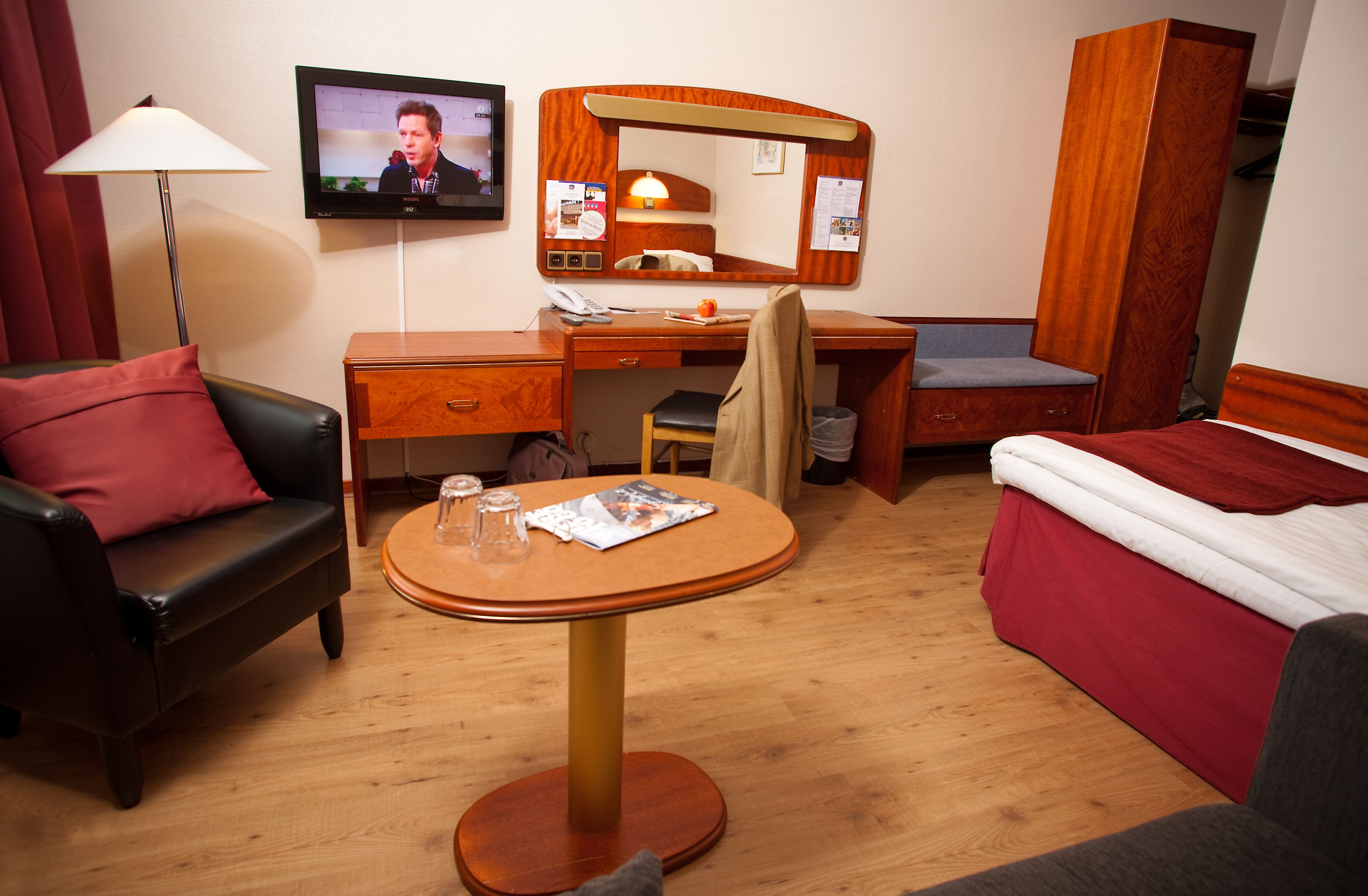 Une chambre d’hôtel avec un bureau en bois, une table ronde, un lit, une télévision et une armoire.