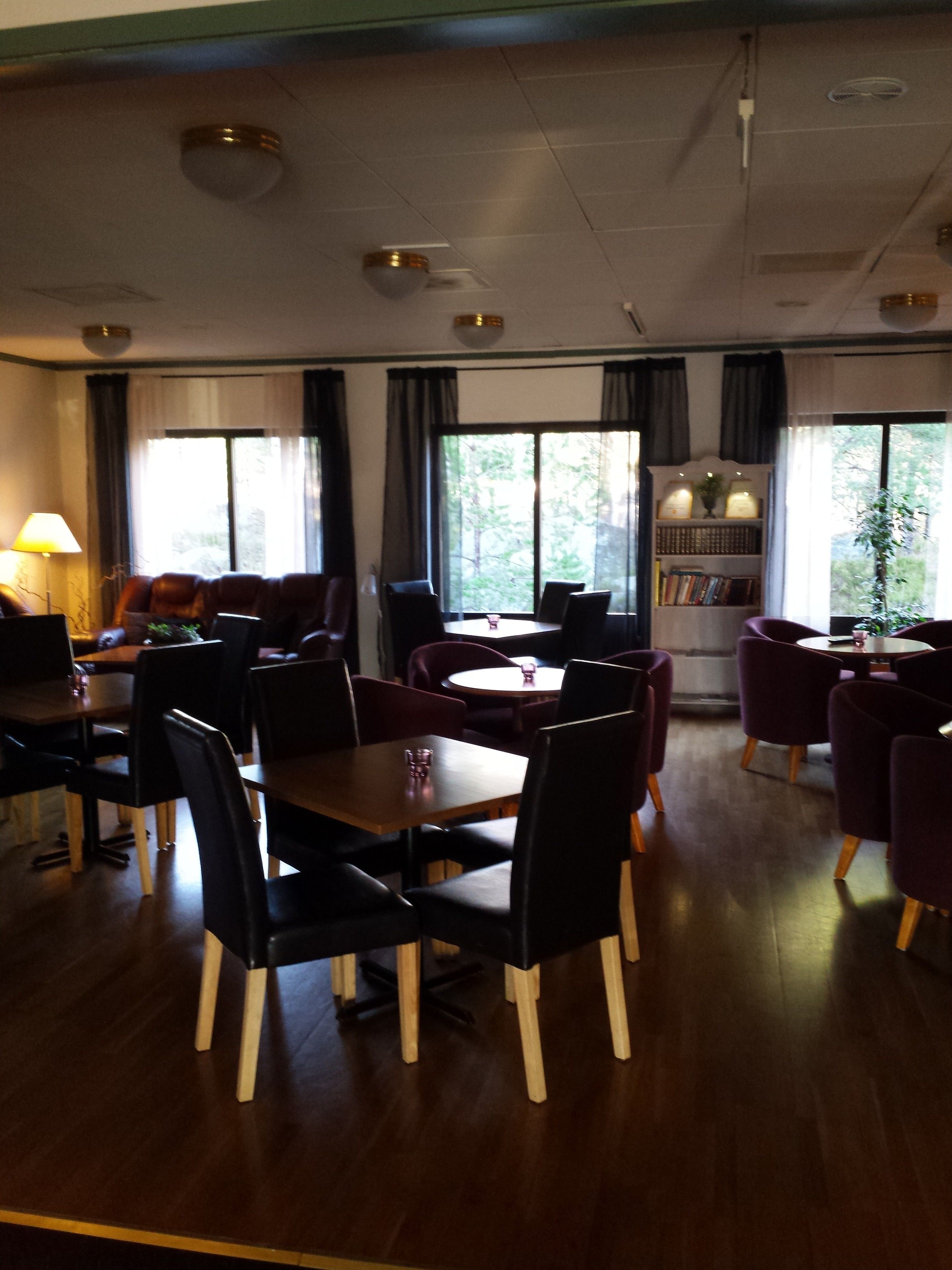 A dining area with tables and chairs, a bookshelf, and large windows with curtains.