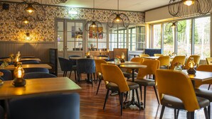 L’intérieur d’un restaurant avec des tables en bois, des chaises jaunes et des luminaires suspendus.