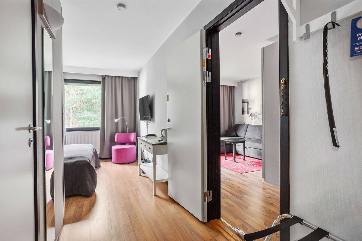 A modern hotel room with a bed, a desk, a chair, a TV, and a view of the outdoors.