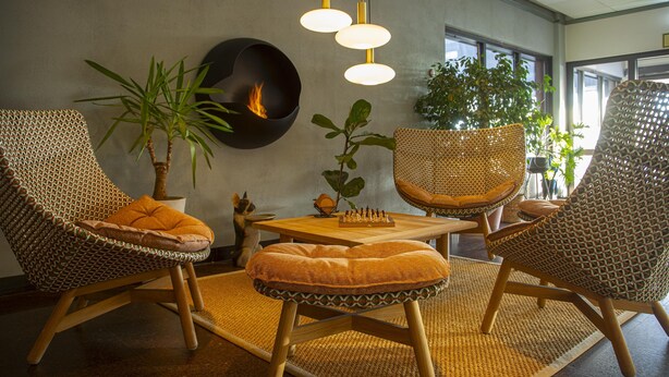 Un intérieur moderne avec des meubles en osier, une cheminée et une lumière naturelle provenant des fenêtres.