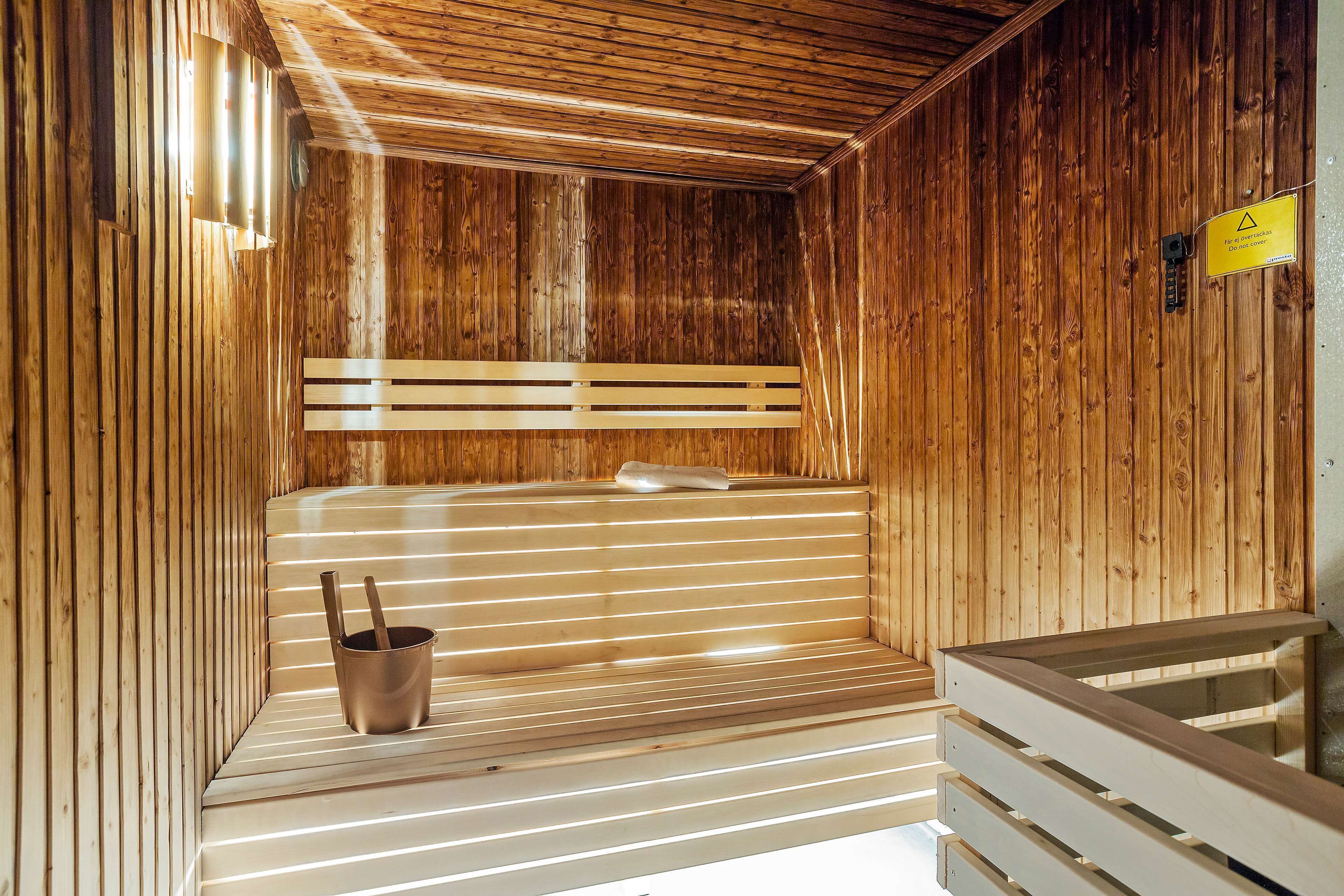 Uma sauna de madeira com bancos, um assento de banco, um porta-toalhas e uma placa indicando o uso da sauna.