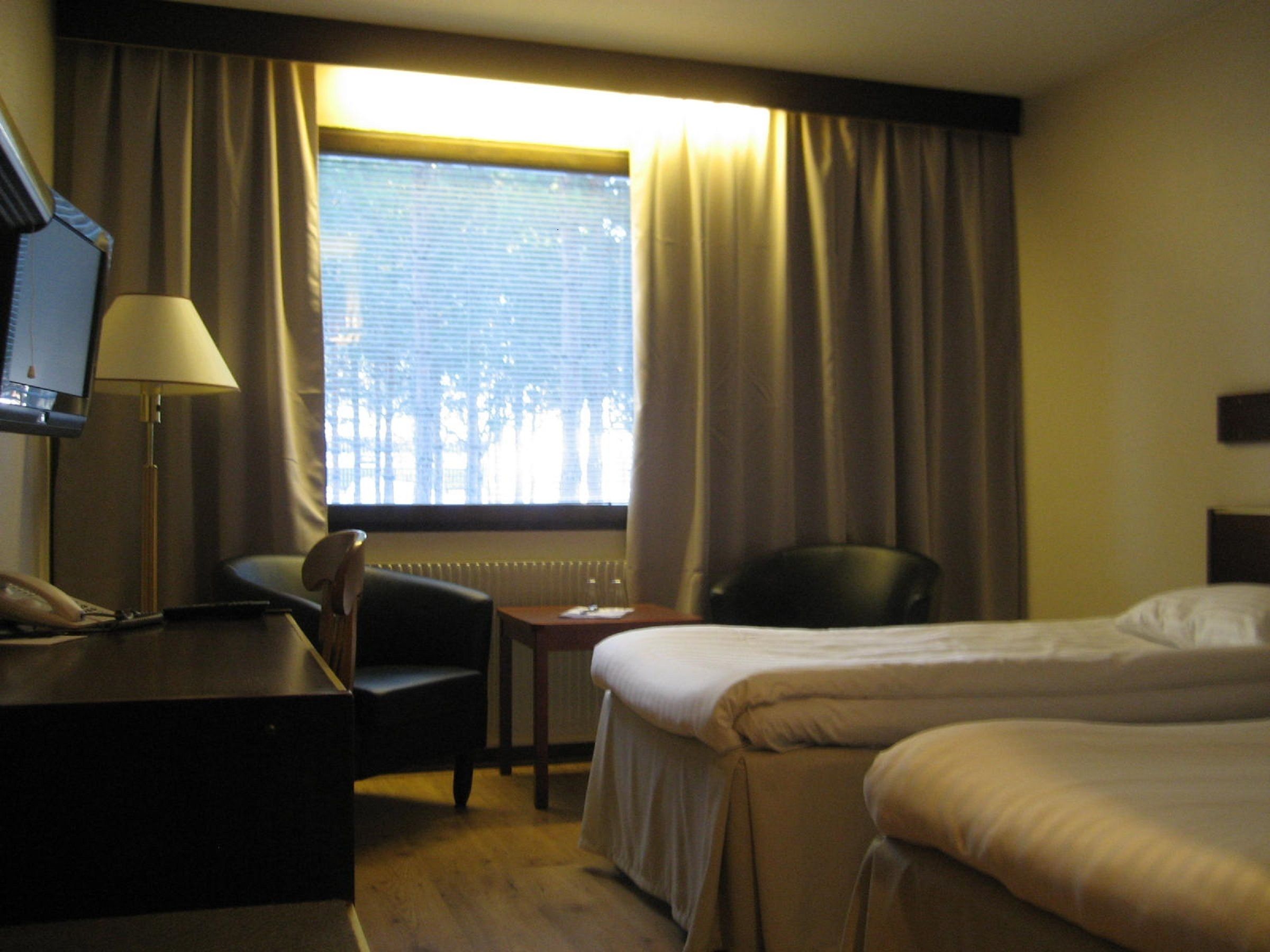 A hotel room with a bed, a desk with a lamp, a chair, and a television.