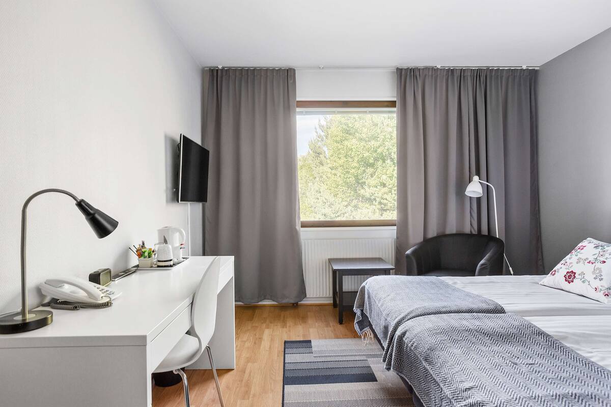 A modern hotel room with a desk, chair, bed, and a large window with curtains.