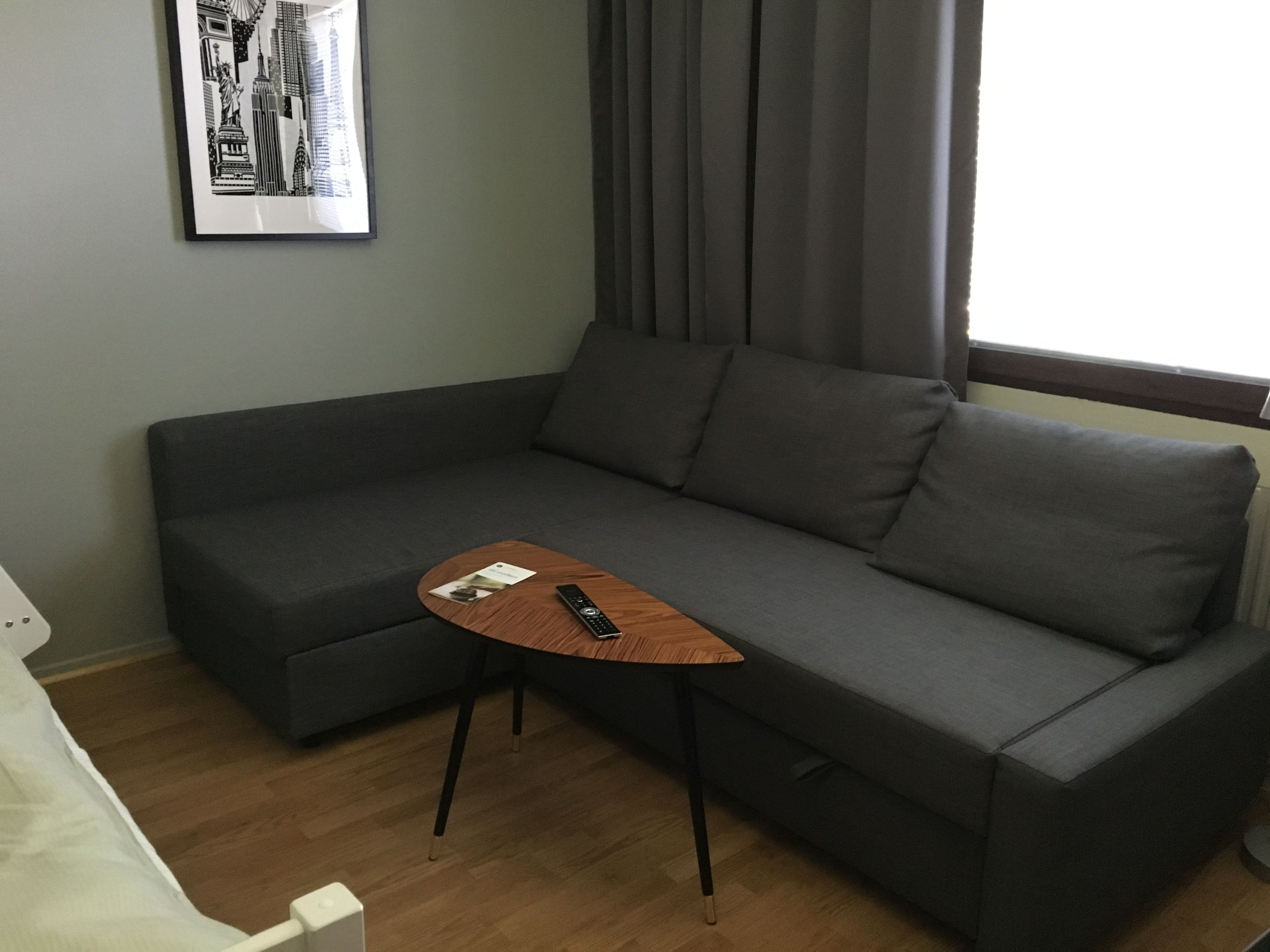 A gray sofa with a small wooden table and a remote control on it.