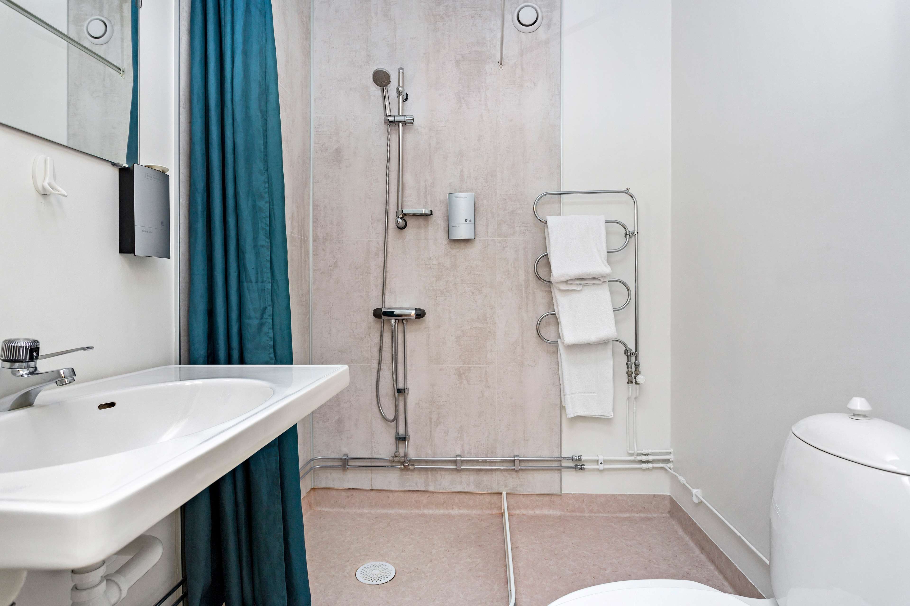 Un baño moderno con un lavamanos blanco, una ducha con cabezal de ducha manual y un inodoro.