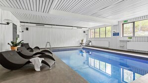 Une piscine avec des chaises longues, une plante en pot et une fenêtre donnant sur des arbres.