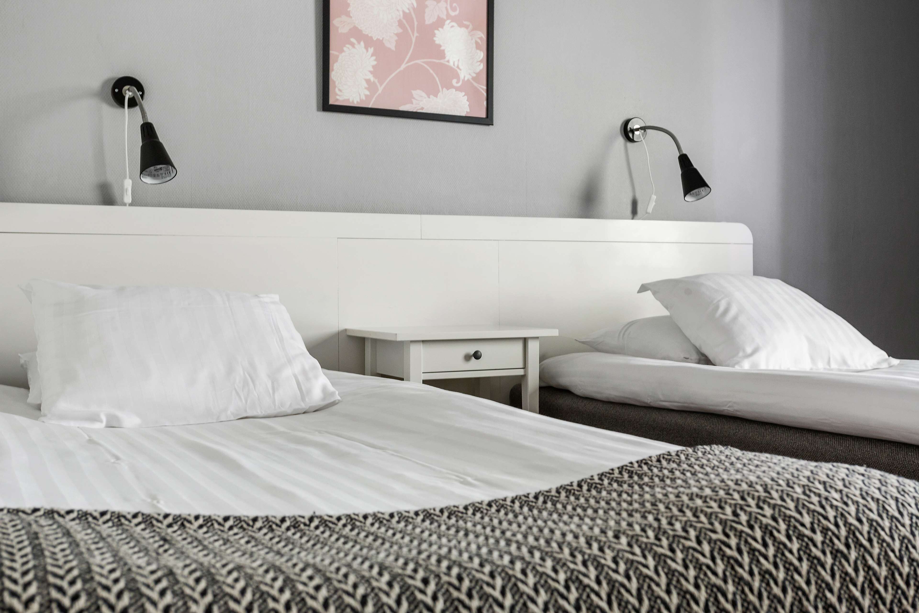 Une chambre d’hôtel avec un lit blanc, une table de chevet, une petite table et deux lampes fixées au mur.