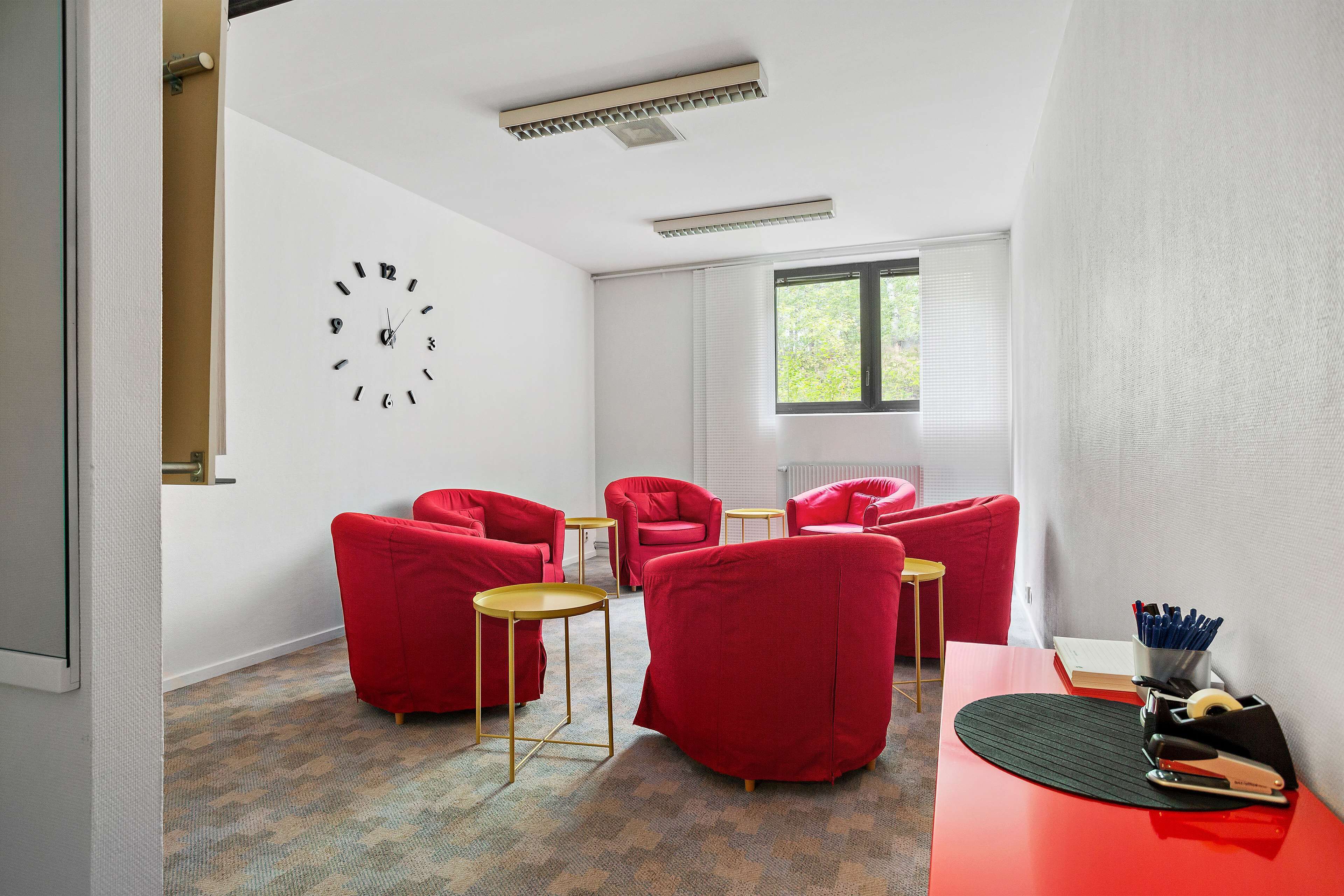A modern room with a red sofa set, a small round table, and a wall clock.