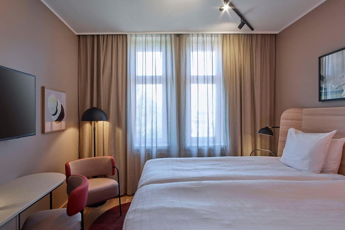 A hotel room with a bed, a desk, a chair, and a TV.