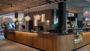 A modern reception area with a wooden reception desk, hanging light fixtures, and a glass display case. - Scandic Strömmen (Norrköping)