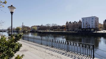 A riverside walkway with a black iron railing, a lamp post, and buildings in the background.