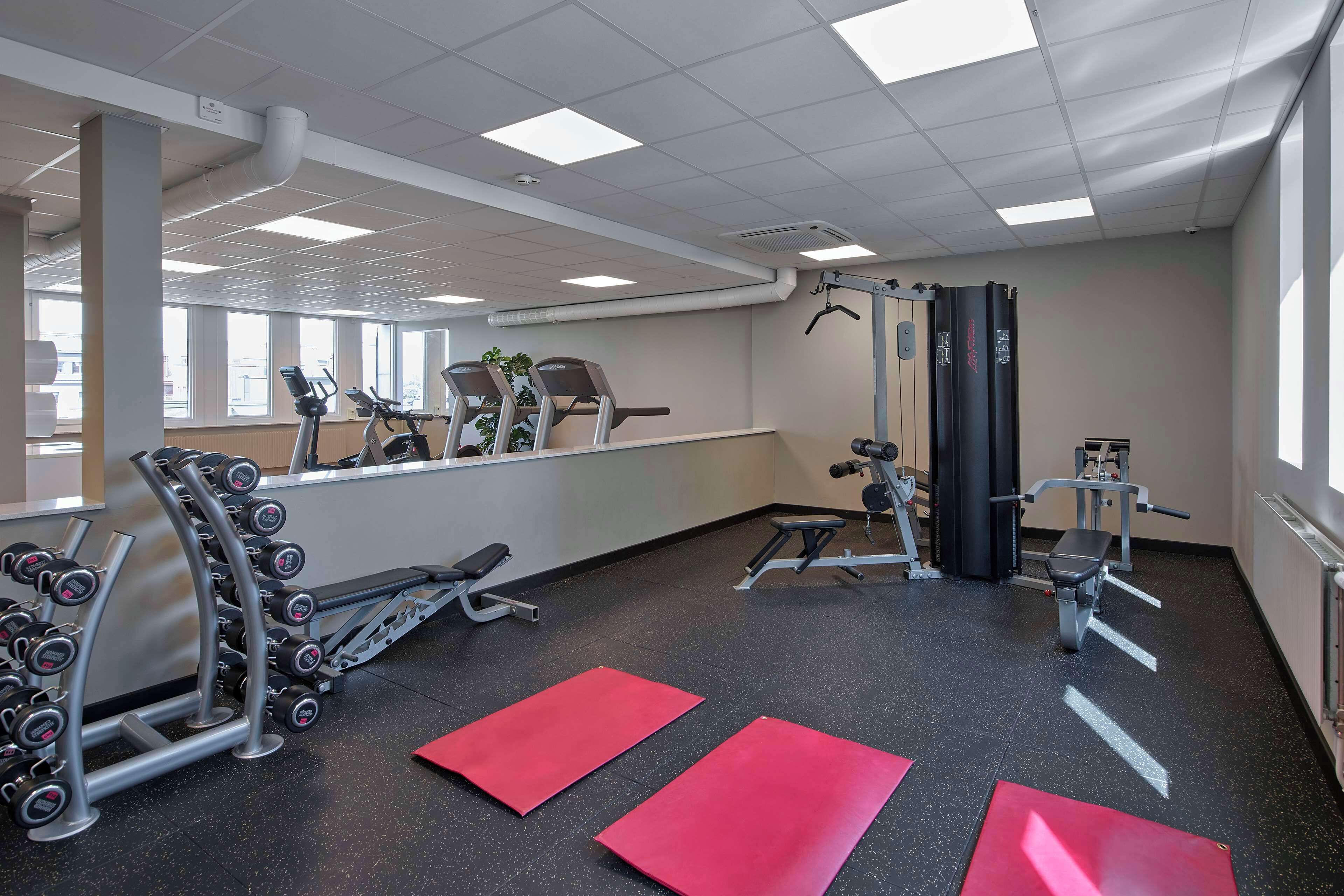 Un gimnasio con equipo de ejercicio, colchonetas rojas y ventanas amplias.