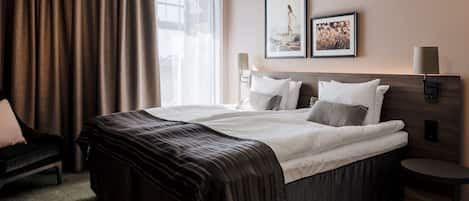 Una habitación de hotel con una cama grande, una silla, una mesita de noche y una ventana con cortinas.