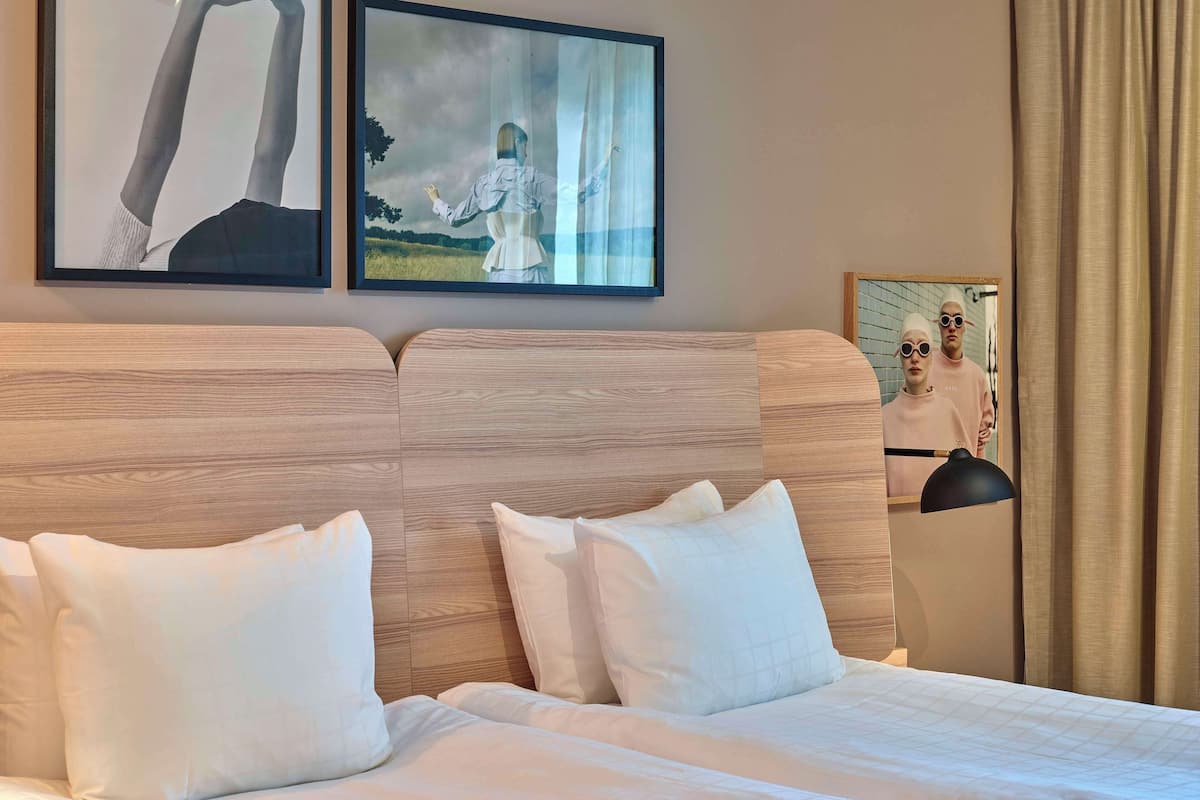 A hotel room with a wooden headboard, white bedding, and two framed artworks on the wall.