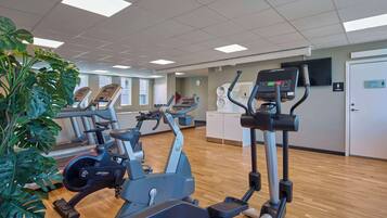 Centro de fitness com bicicletas ergométricas, esteiras e uma grande planta.