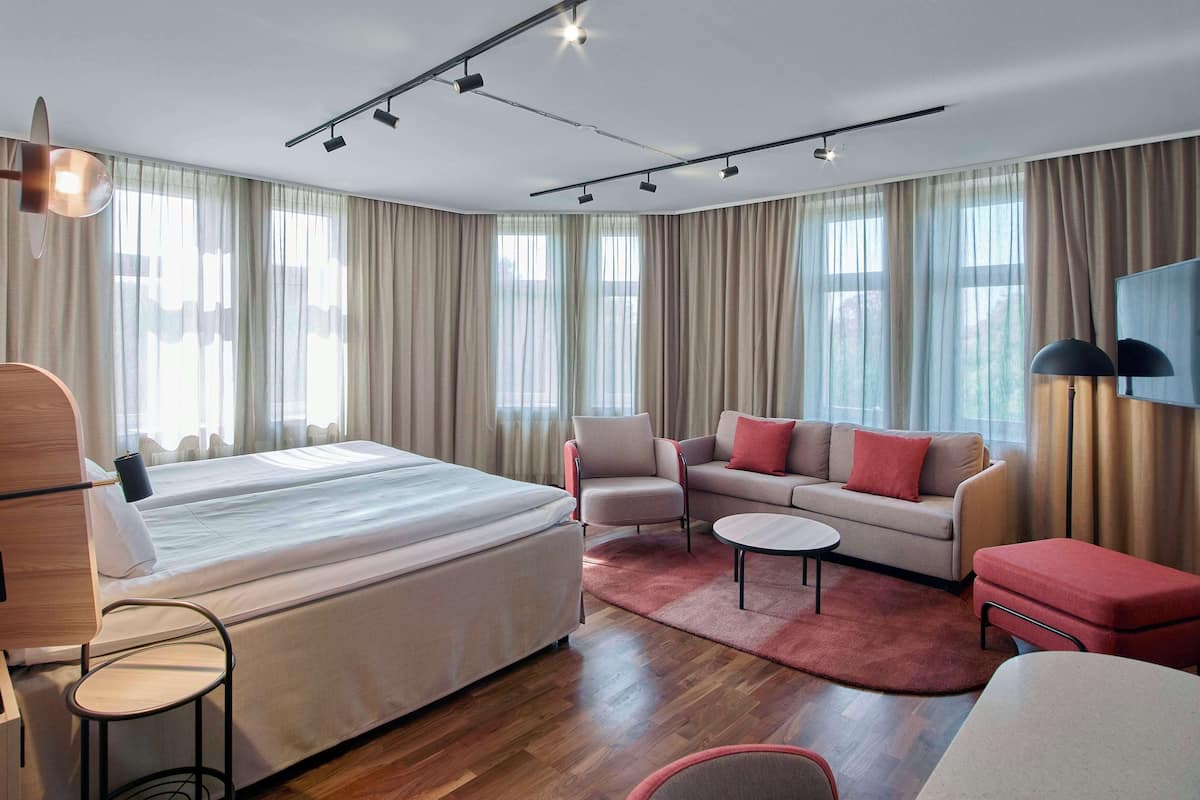 A modern hotel room with a large bed, a sofa, a small table, and a TV.