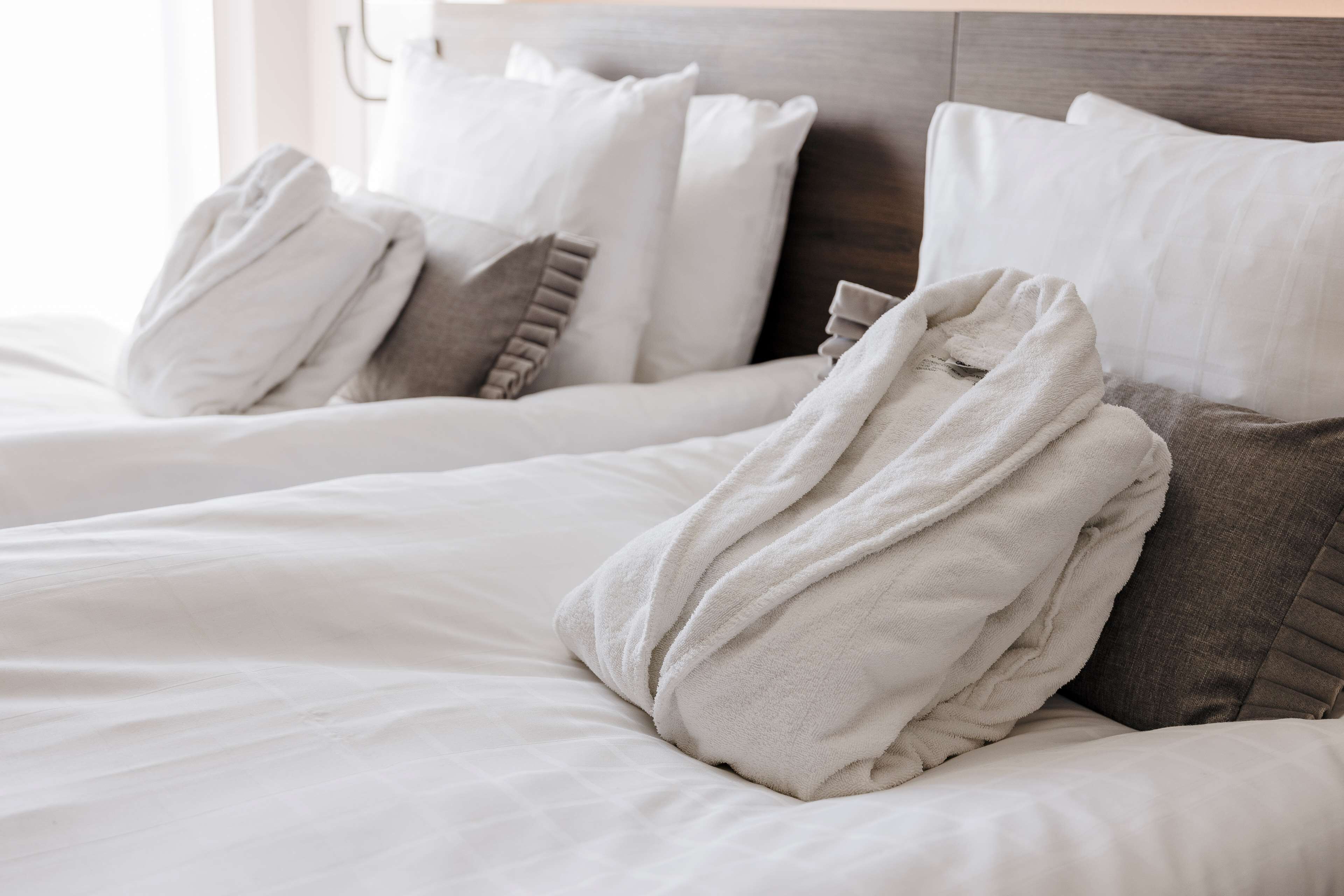 A neatly made bed with white and gray bedding, including a folded bathrobe and pillows.