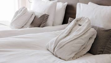 A neatly made bed with white and gray bedding, including a folded bathrobe and pillows.