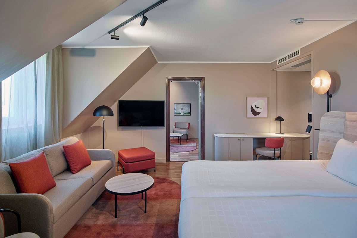 A modern hotel room with a sofa, a bed, a desk, and a TV.