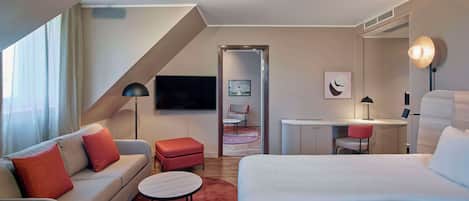 A modern hotel room with a sofa, a bed, a desk, and a TV.