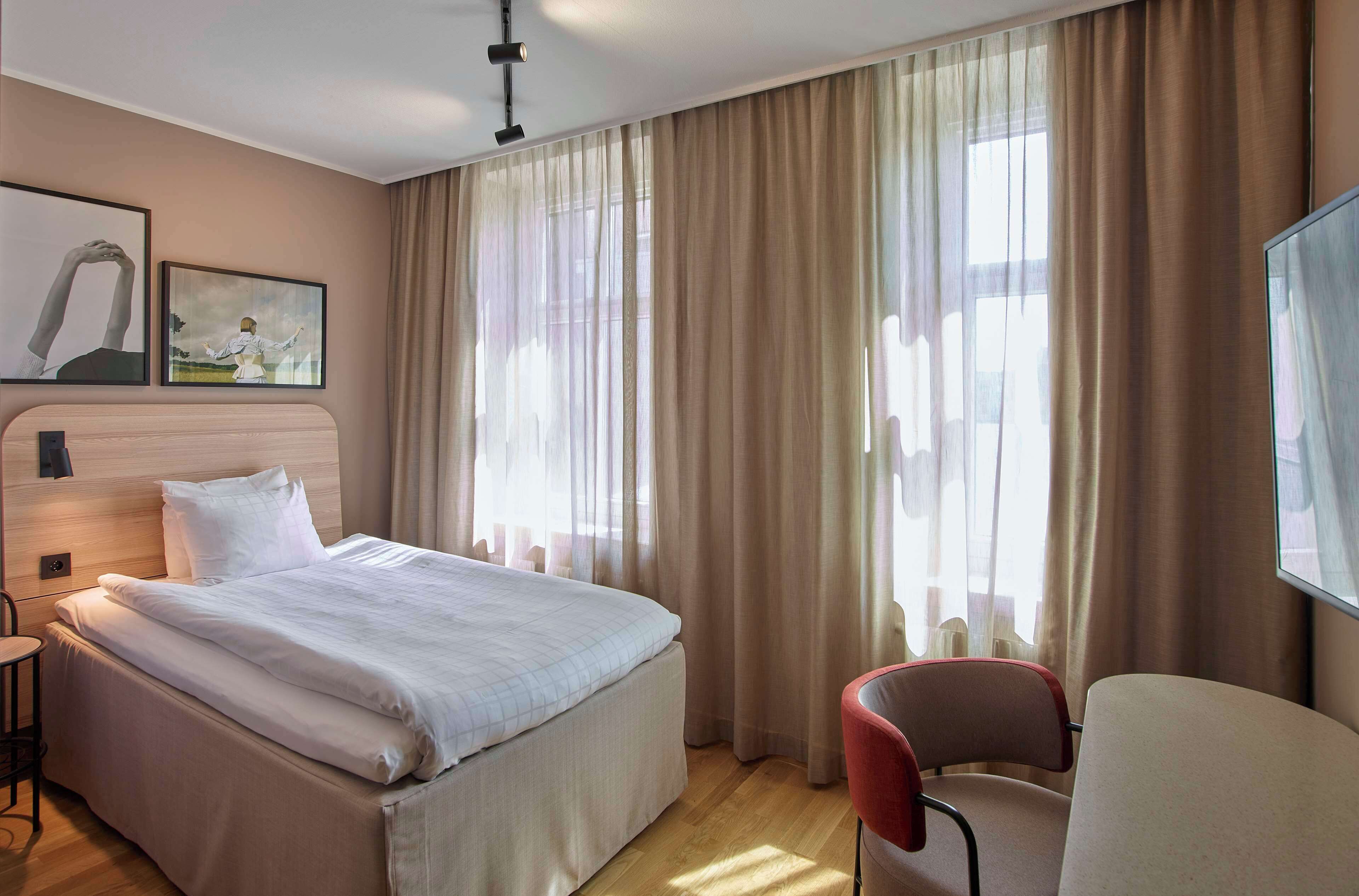 A hotel room with a bed, a chair, and a large window with curtains.