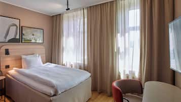 A hotel room with a bed, a chair, and a large window with curtains.