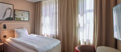 A hotel room with a bed, a chair, and a large window with curtains.