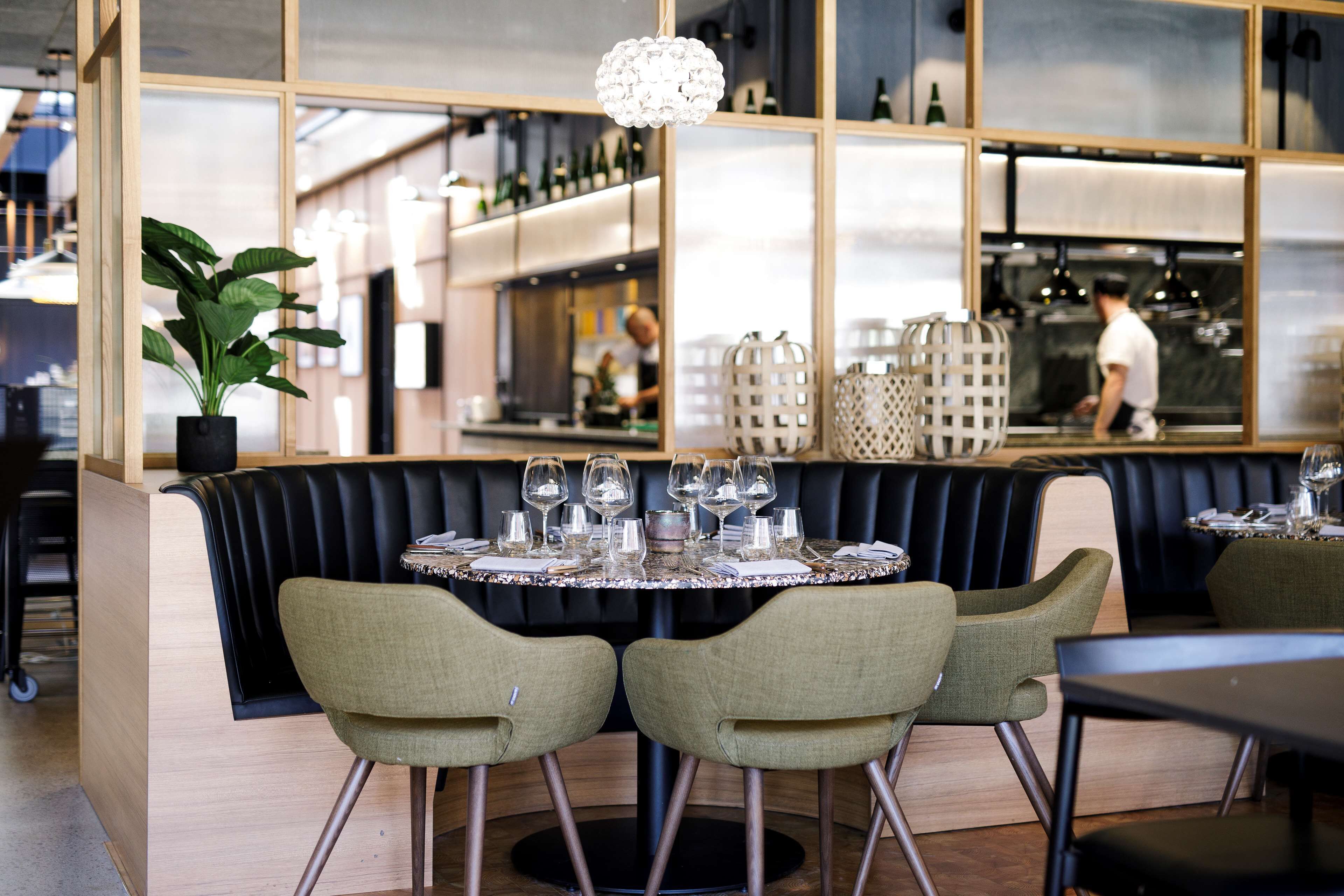 Un restaurante con una mesa redonda para dos, un asiento tapizado negro y una planta en maceta.