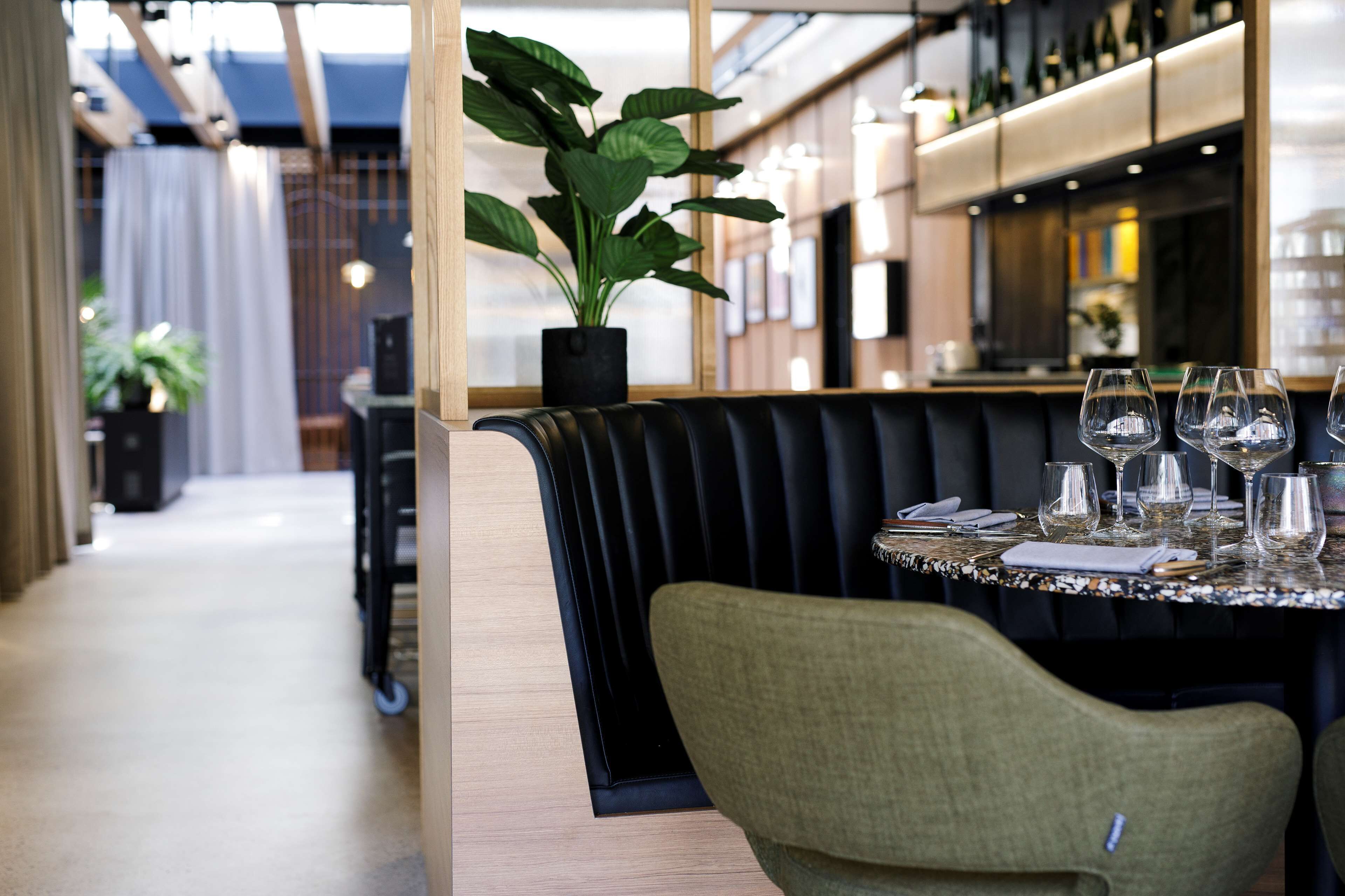 Un restaurante con una zona de asientos tipo cabina, una planta en maceta y un bar al fondo.