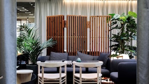 A modern lounge area with a sofa, two wooden chairs, a small table, and potted plants. - Scandic Strömmen (Norrköping)