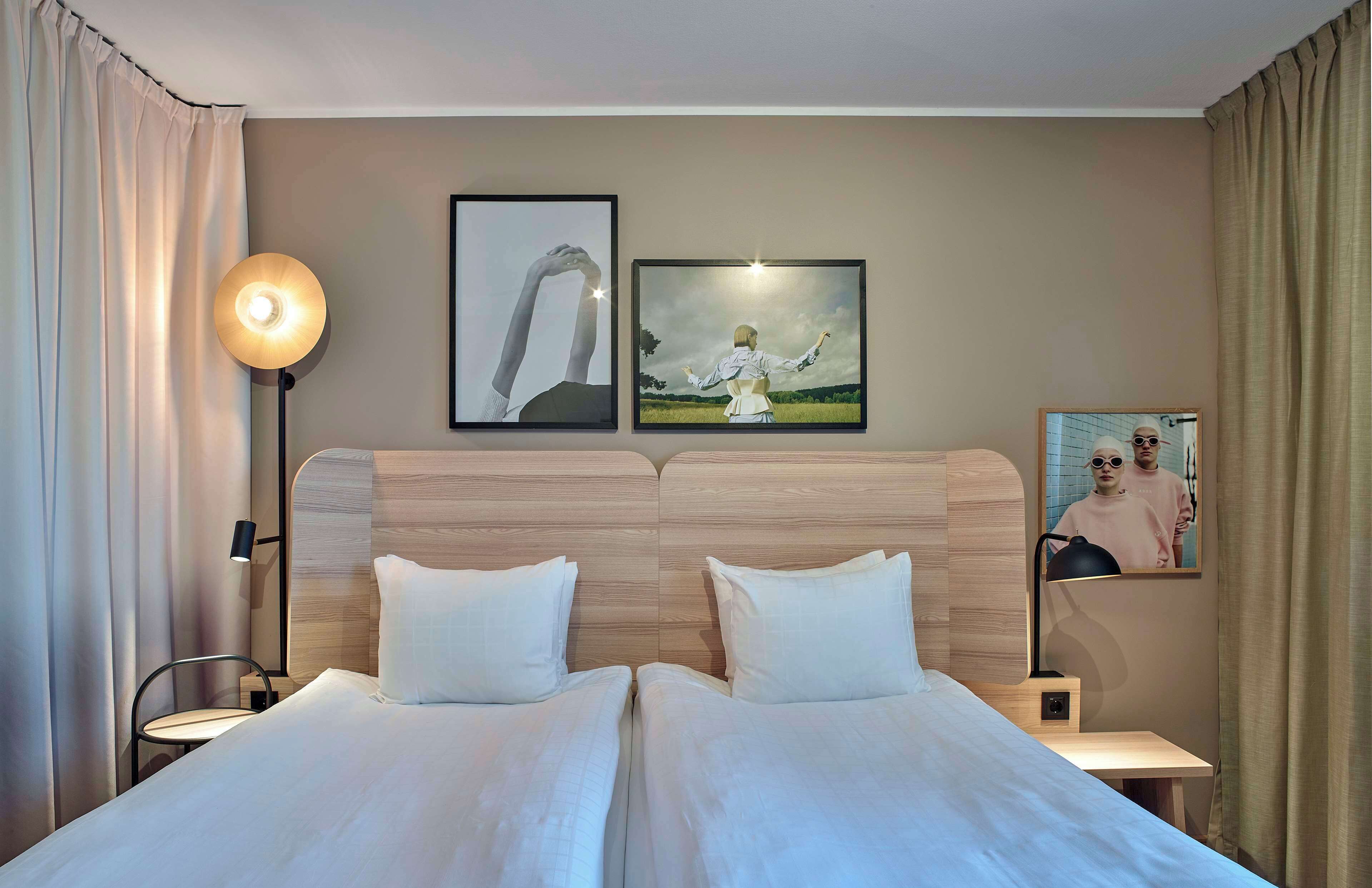 Una cama doble con sábanas blancas, una mesita de noche con lámpara y dos cuadros enmarcados en la pared.