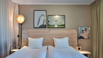 Una cama doble con sábanas blancas, una mesita de noche con lámpara y dos cuadros enmarcados en la pared.